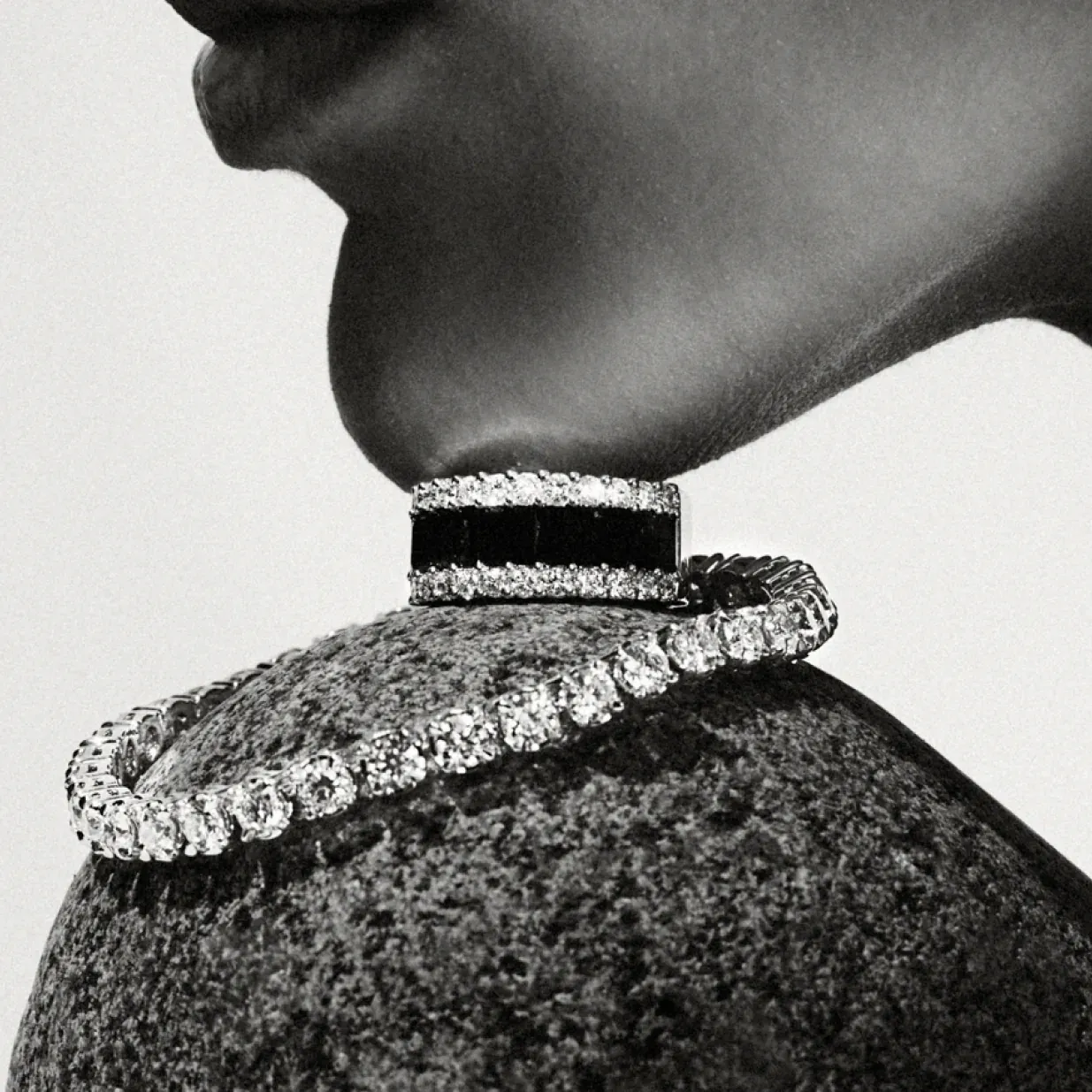 Elegant black choker and diamond necklace on a person's neck, monochrome style.