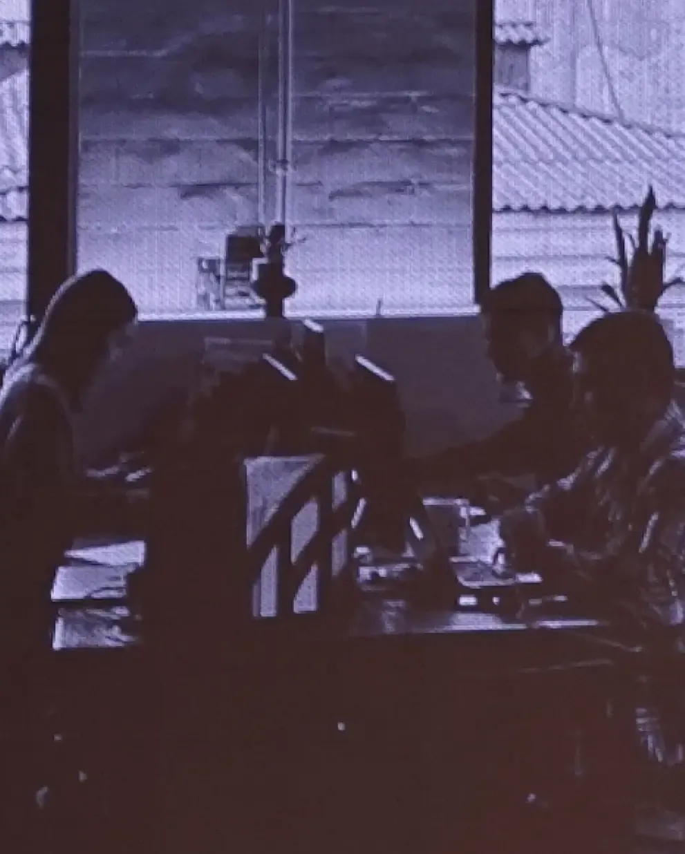 Group of people silhouetted, working or socializing around a table near a window.