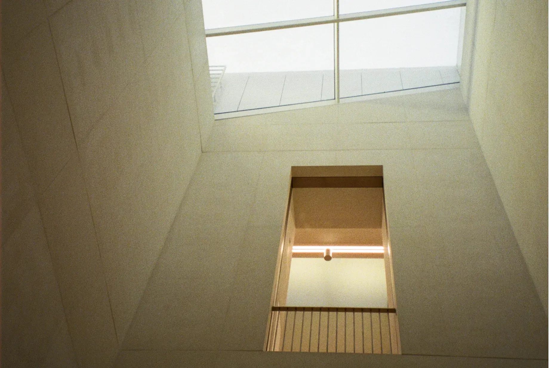 Architectural interior looking up at a bright skylight and an open stairwell with a railing.