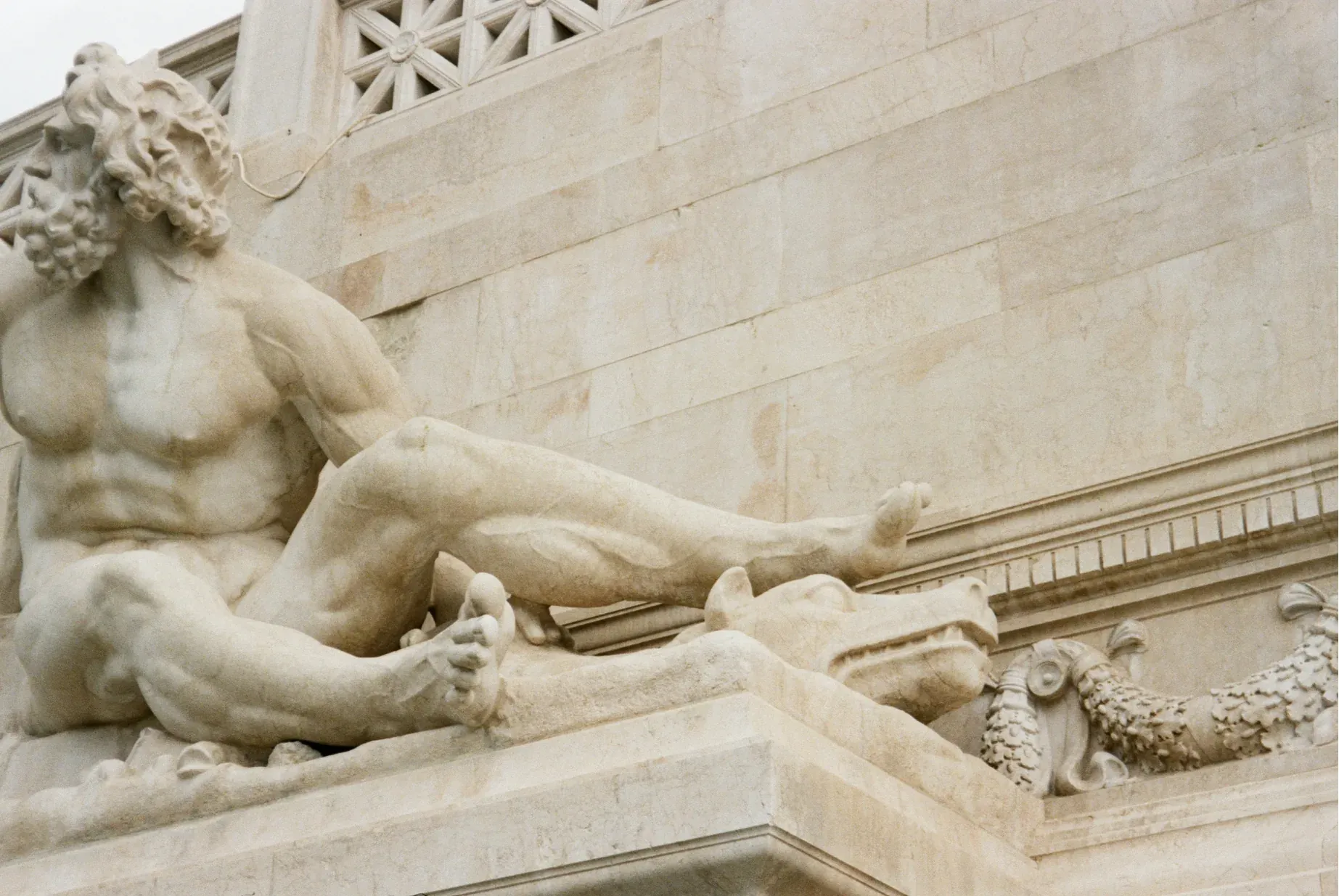 Detailed marble statue of a bearded, muscular man reclining on an ornate stone monument.