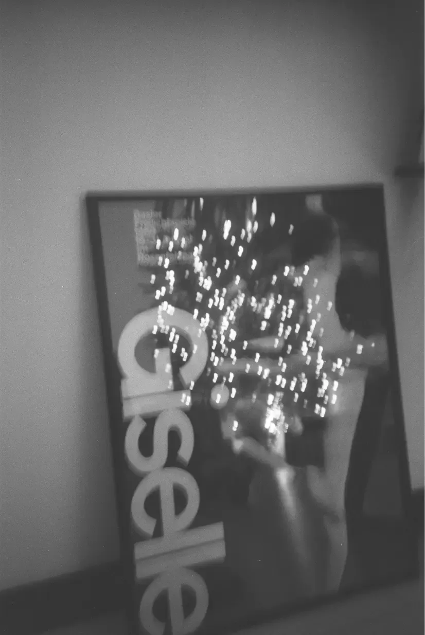 Black and white poster titled 'Giselle' with a figure and sparkling lights, leaning against a wall.