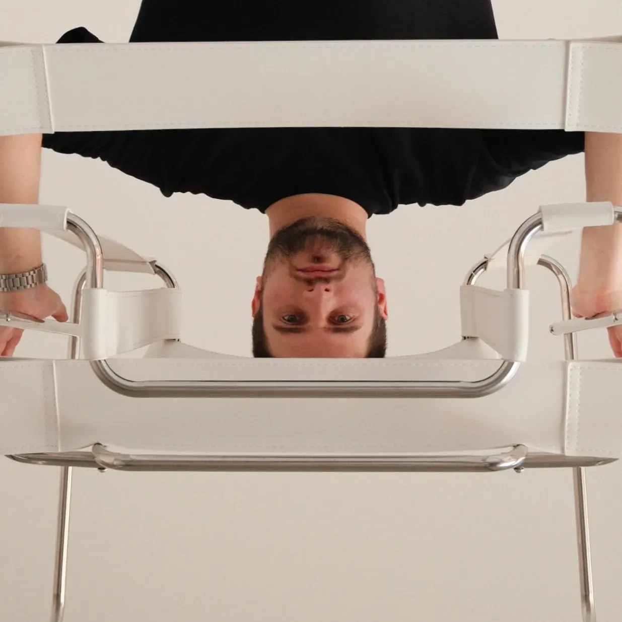 Man's head and shoulders upside down, framed by white metal structures, hands gripping.