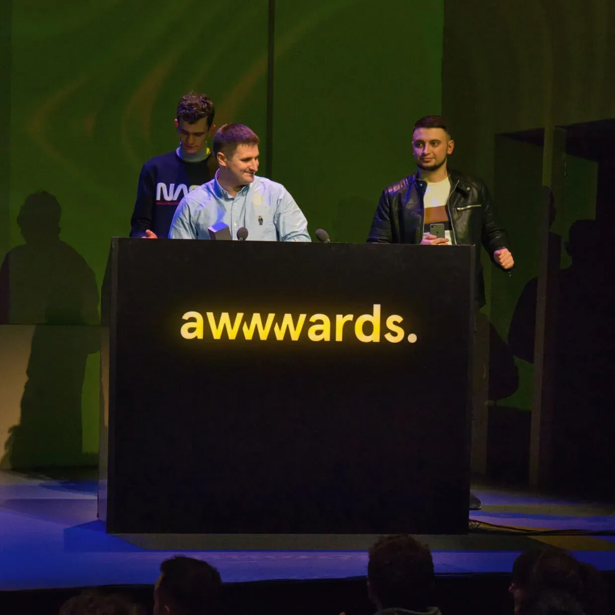 Three individuals stand behind an 'awwwards.' podium on a stage.